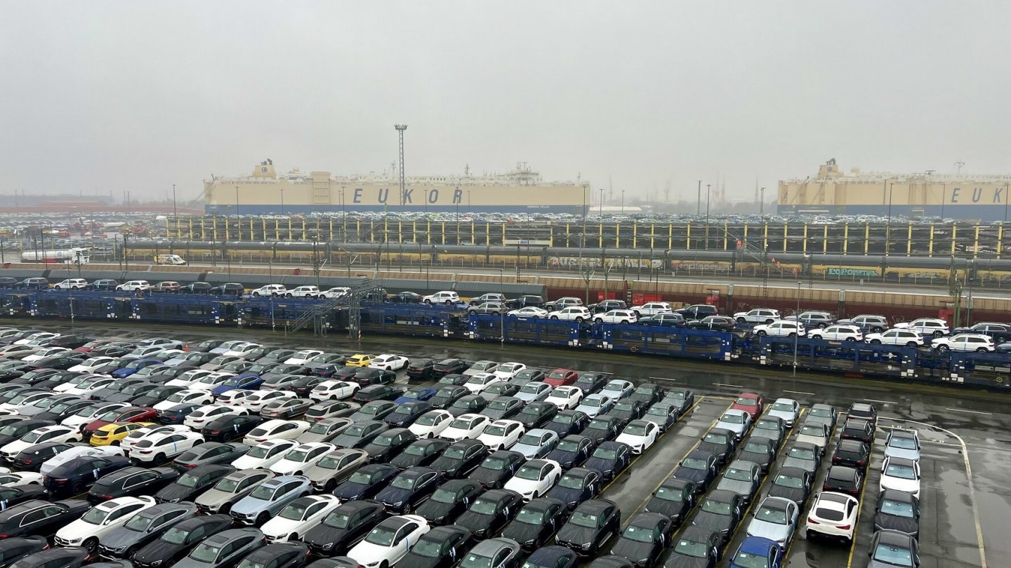 Neuwagen werden auch per Zug an- und abtransportiert. Im Hintergrund ein RoRo-Frachter.